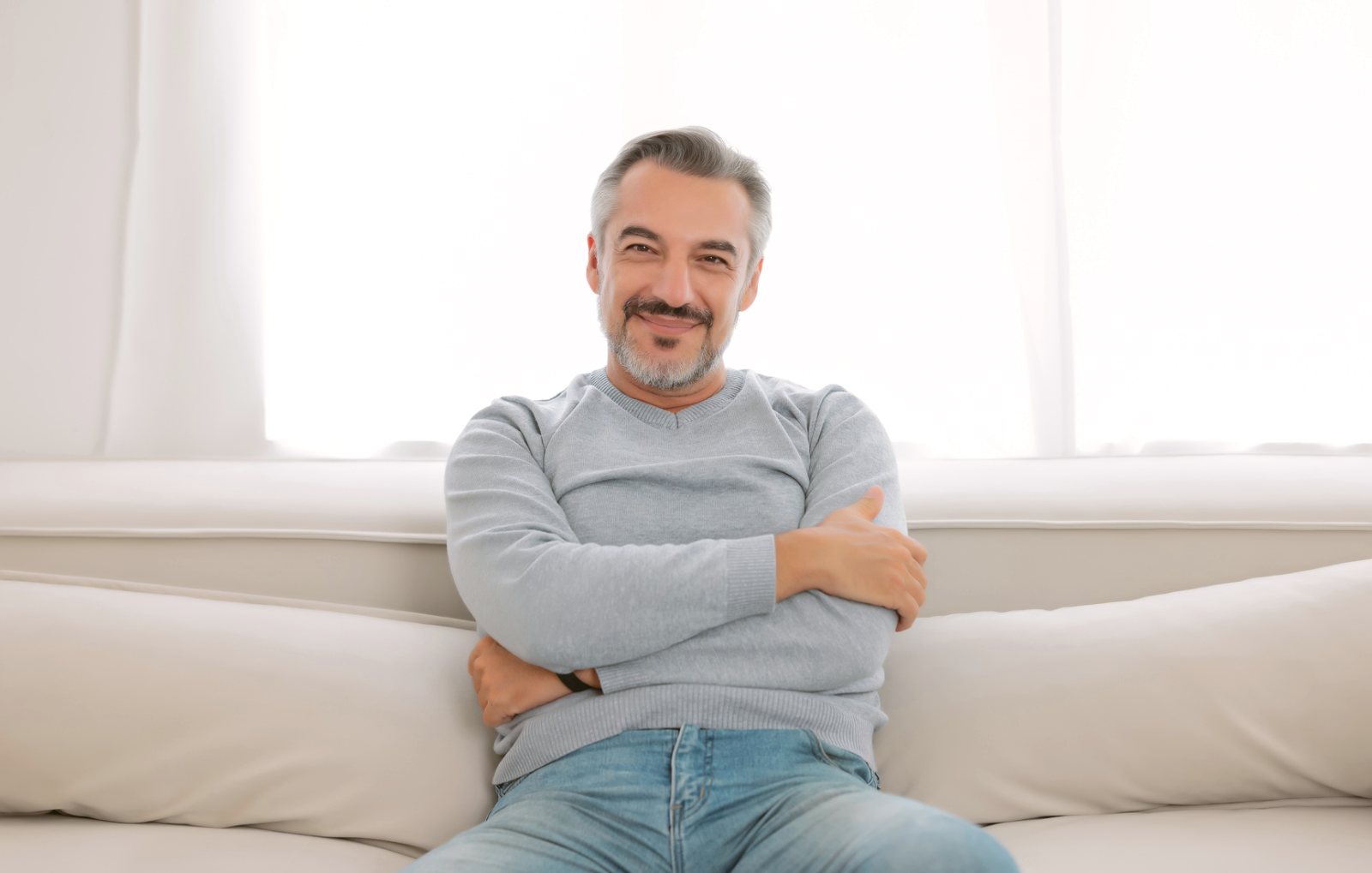 A middle-aged man sitting relaxed and smiling on a sofa in a bright room