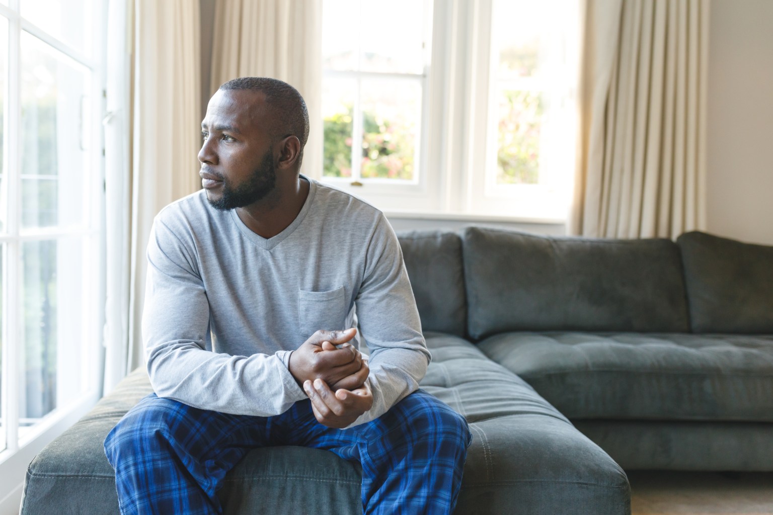 A thoughtful man sitting on a couch looking out the window