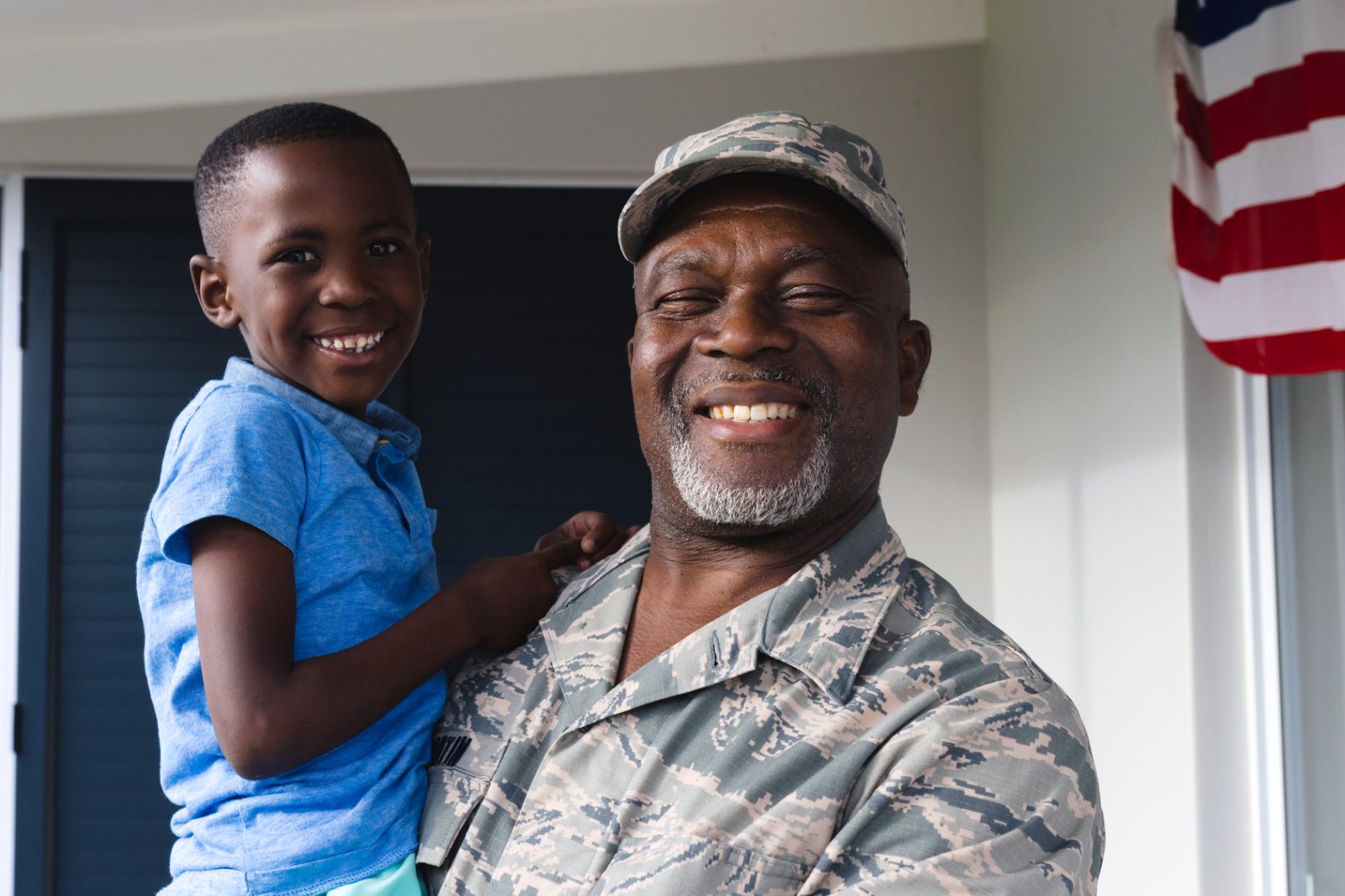 A smiling veteran in uniform holding his grandson at home